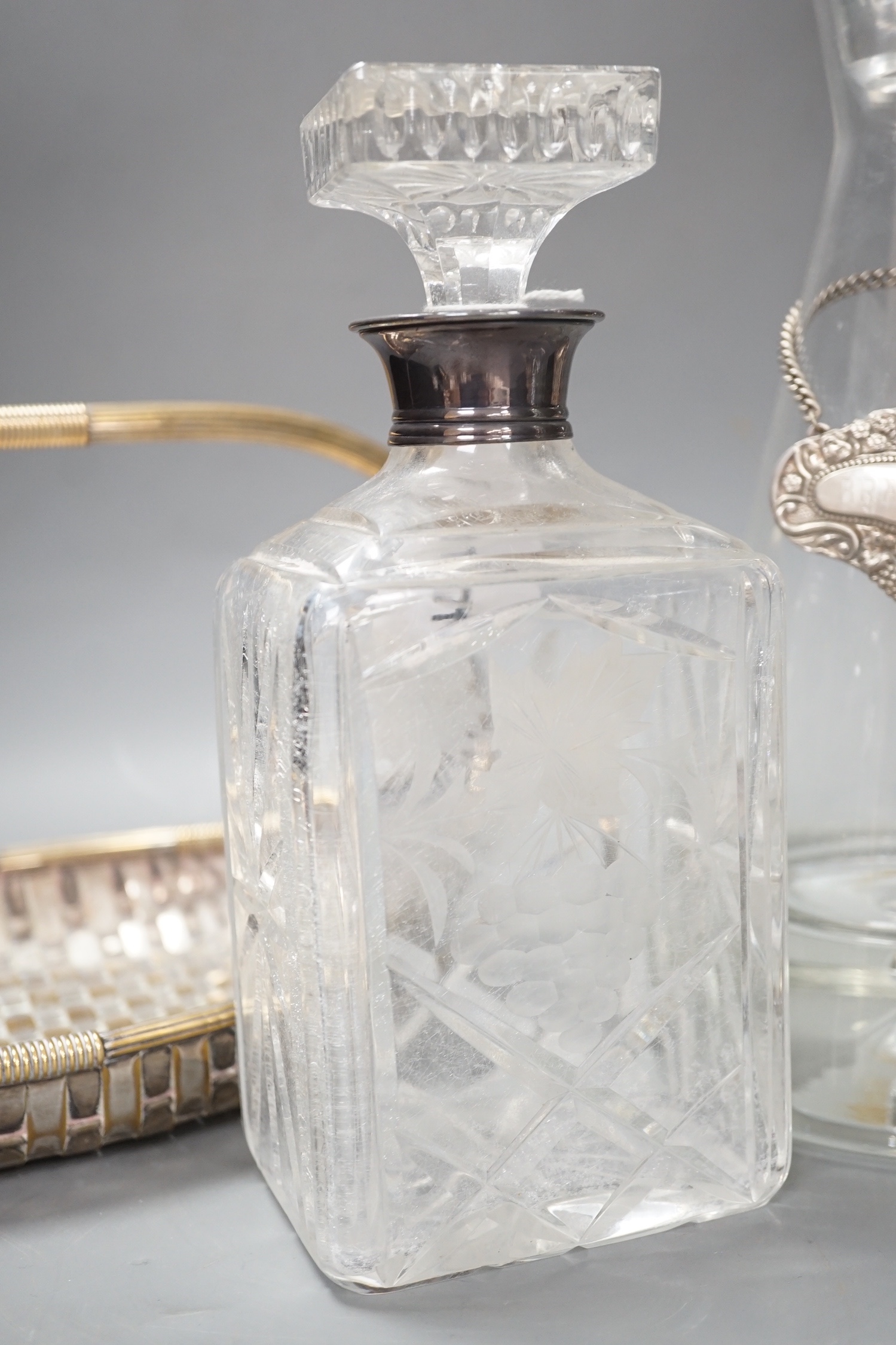 A silver topped decanter together with two other assorted decanters, a silver whisky label and a silver plated basket